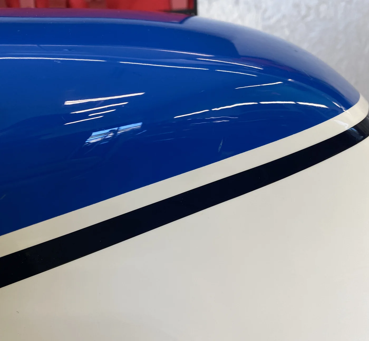 A dent at the stripe of a blue and white motorcycle tank after paintless dent repair, factory paint intact