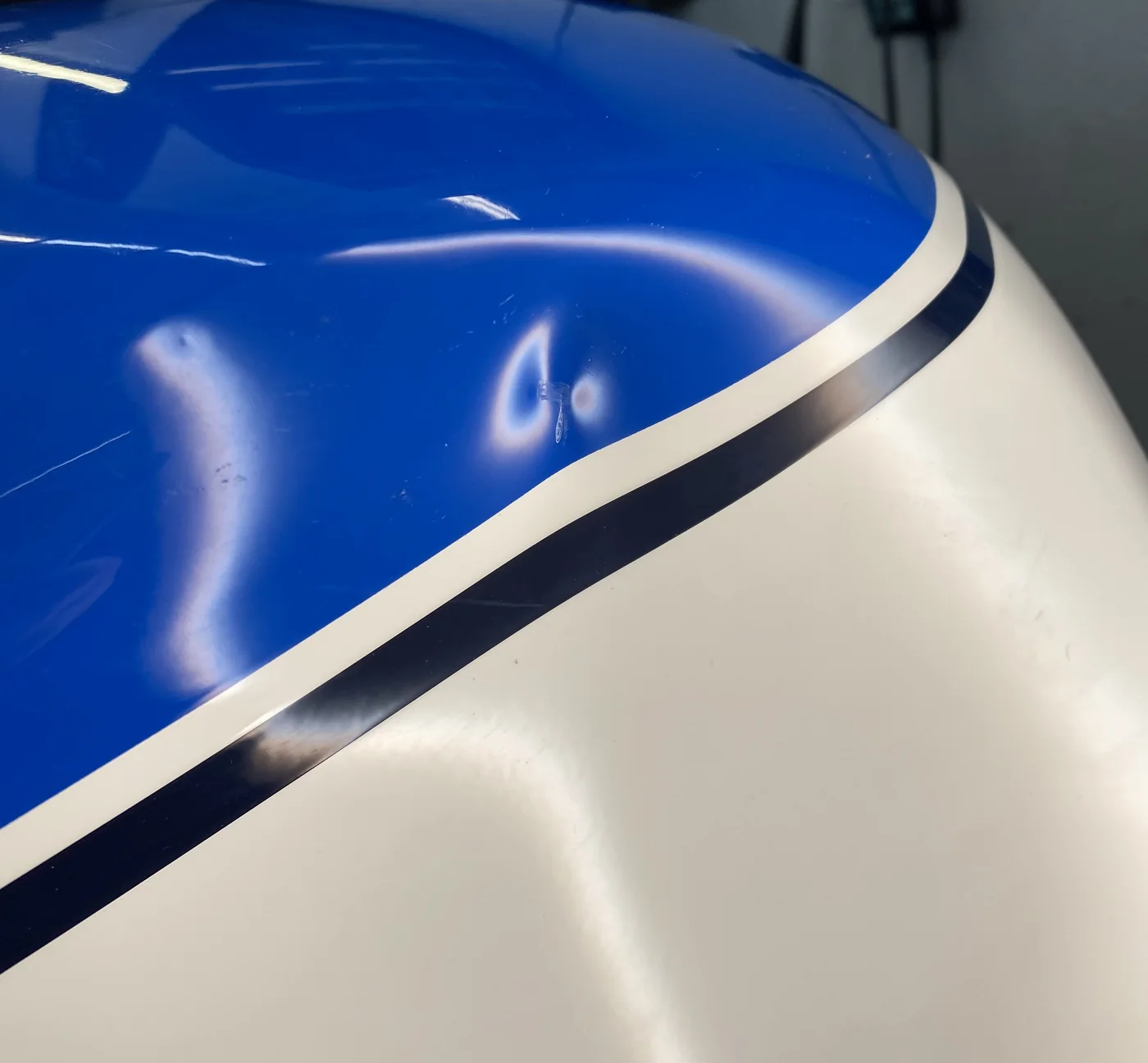 A dent at the stripe of a blue and white motorcycle tank before paintless dent repair