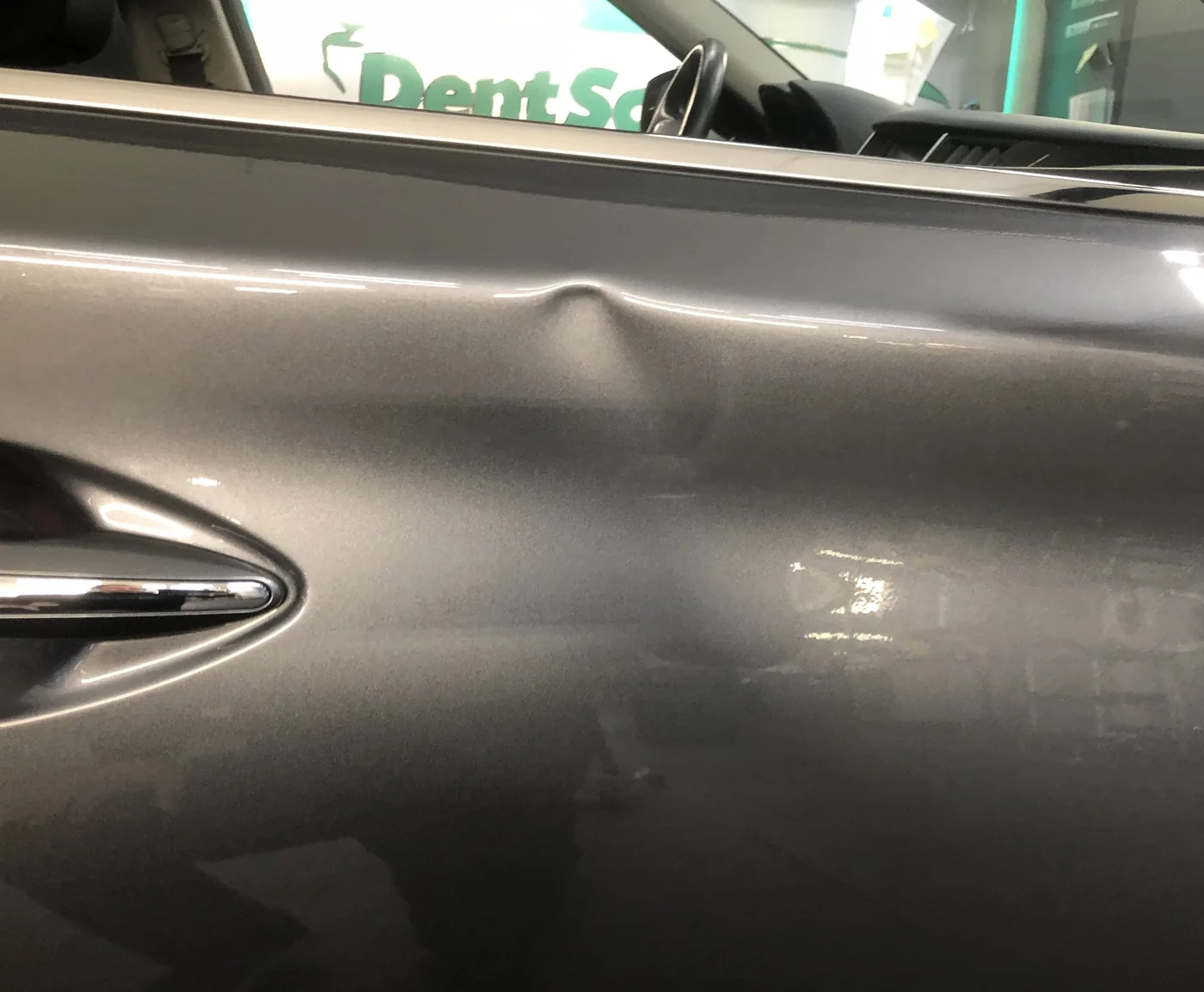A crease above the handle on a gray sedan front door before paintless dent repair