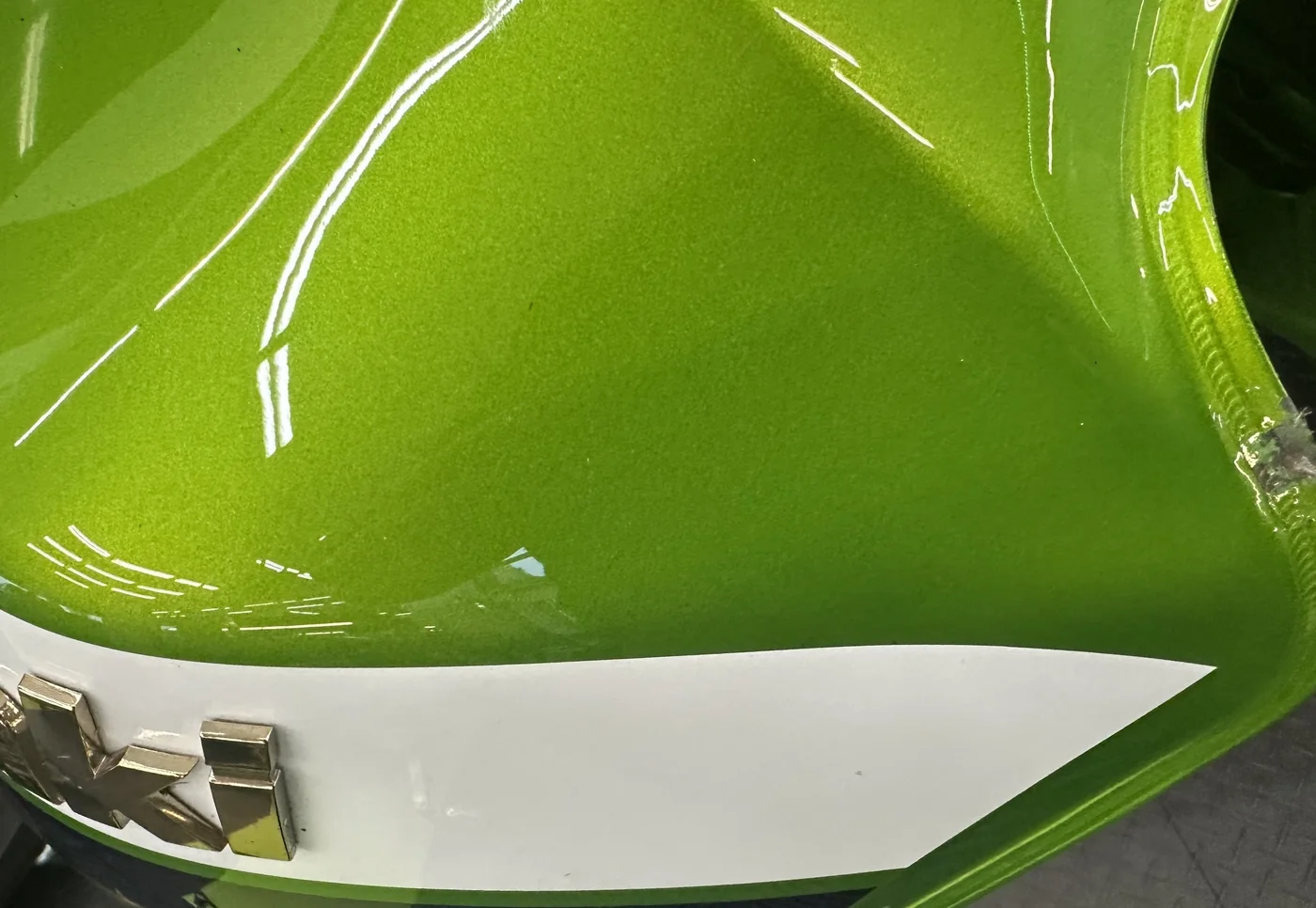 A dent circled on a green sport bike fuel tank after paintless dent repair, factory paint intact