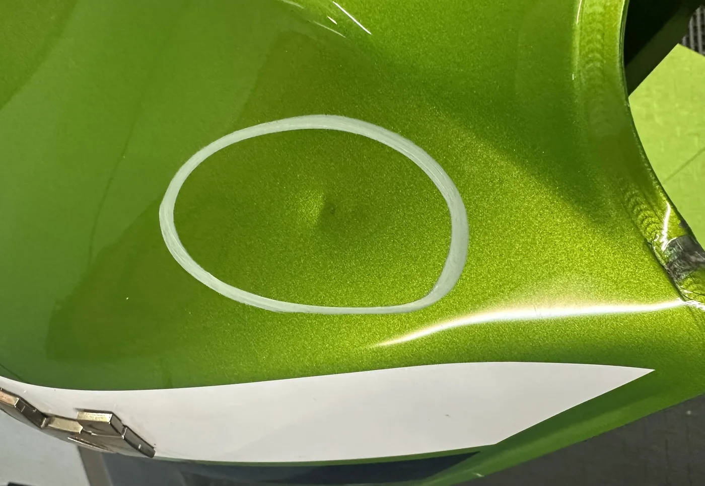 A dent circled on a green sport bike fuel tank before paintless dent repair