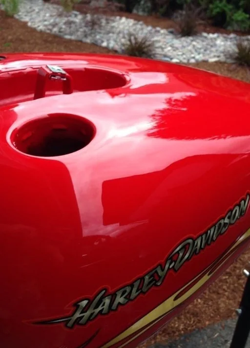 A deep dent in a red Harley-Davidson fuel tank after paintless dent repair, factory paint intact