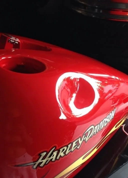 A deep dent in a red Harley-Davidson fuel tank before paintless dent repair