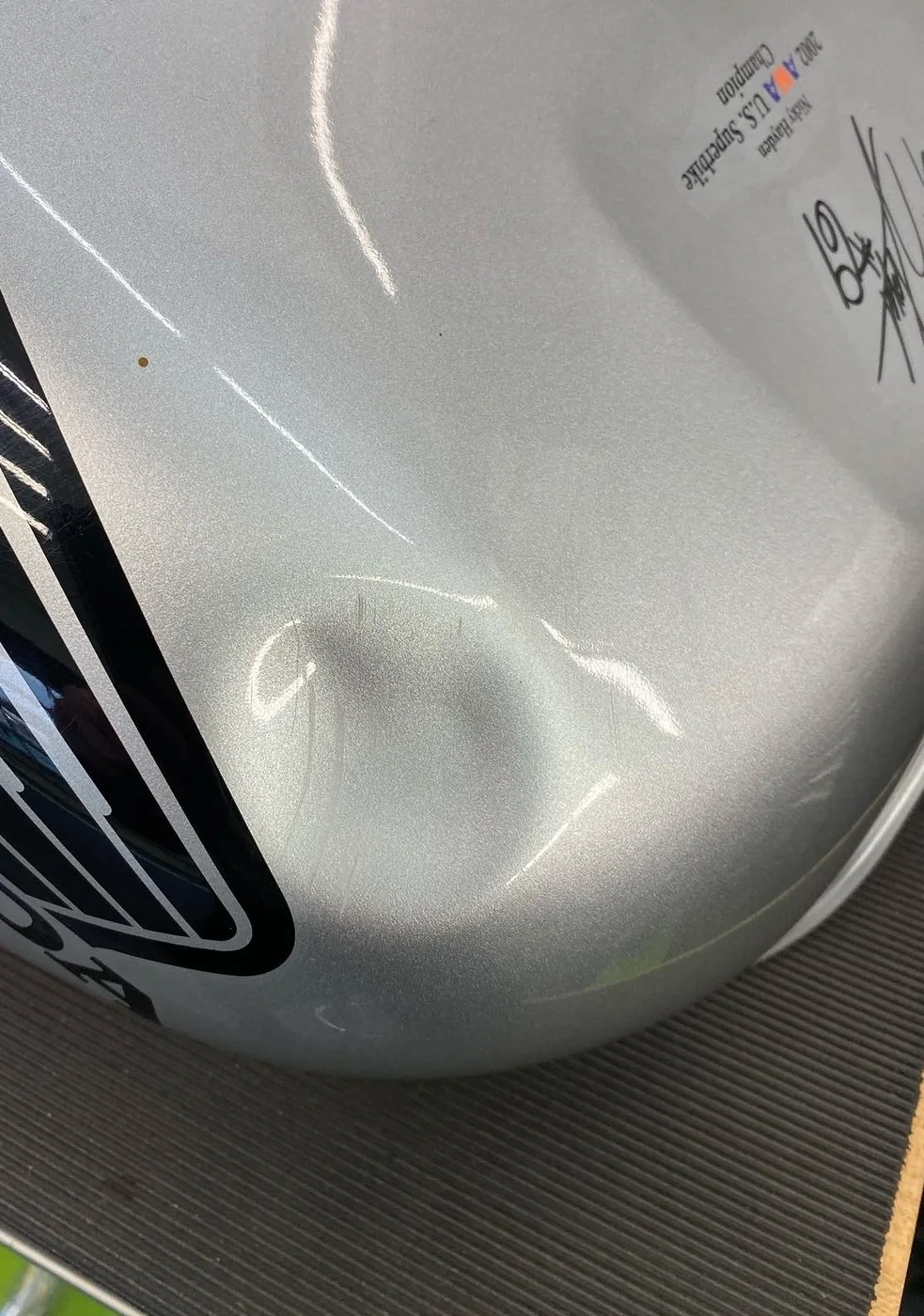 A dent in the silver fuel tank of a Honda motorcycle before paintless dent repair