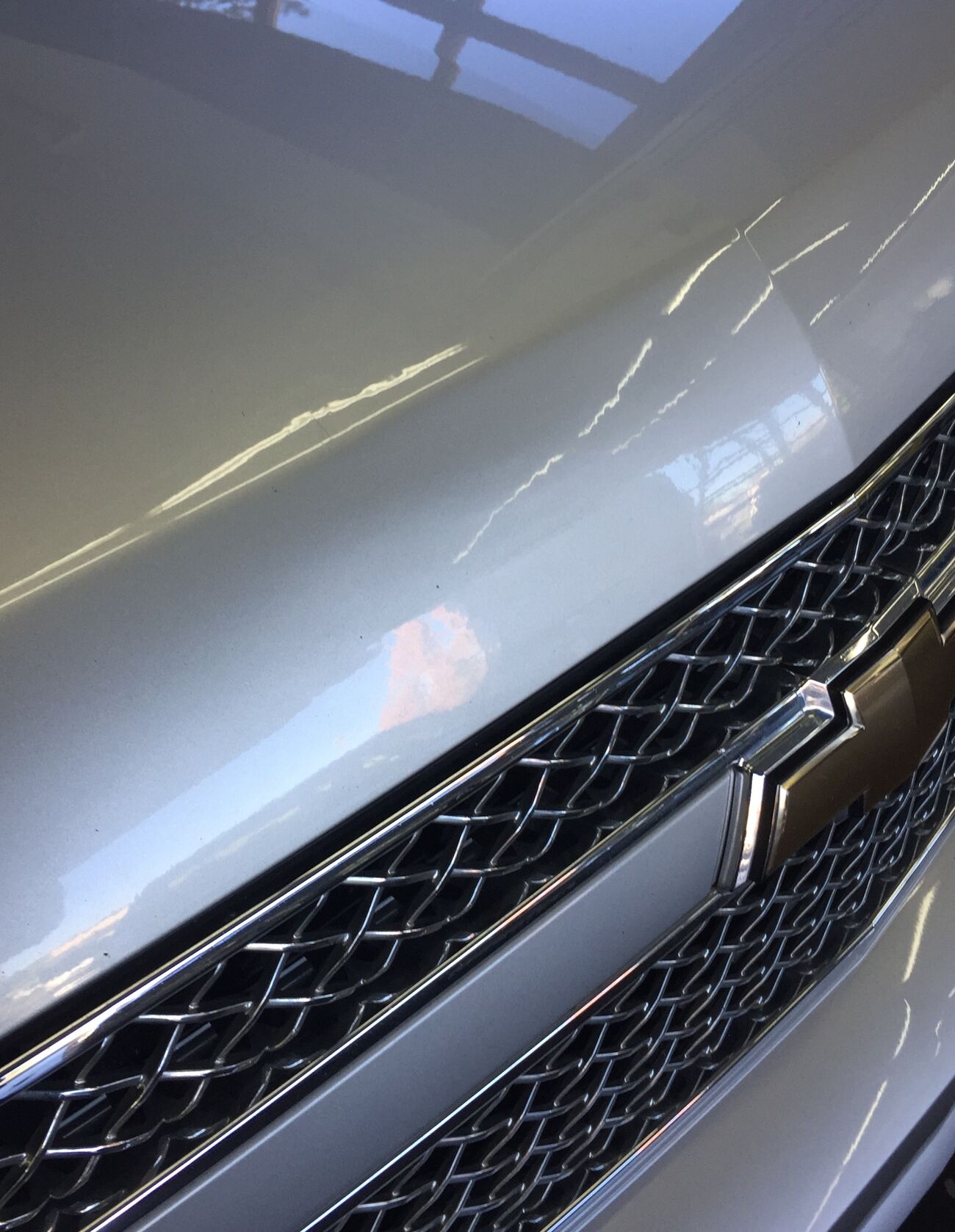 The same silver Chevrolet hood after paintless dent repair, the reflection running straight and the factory paint untouched