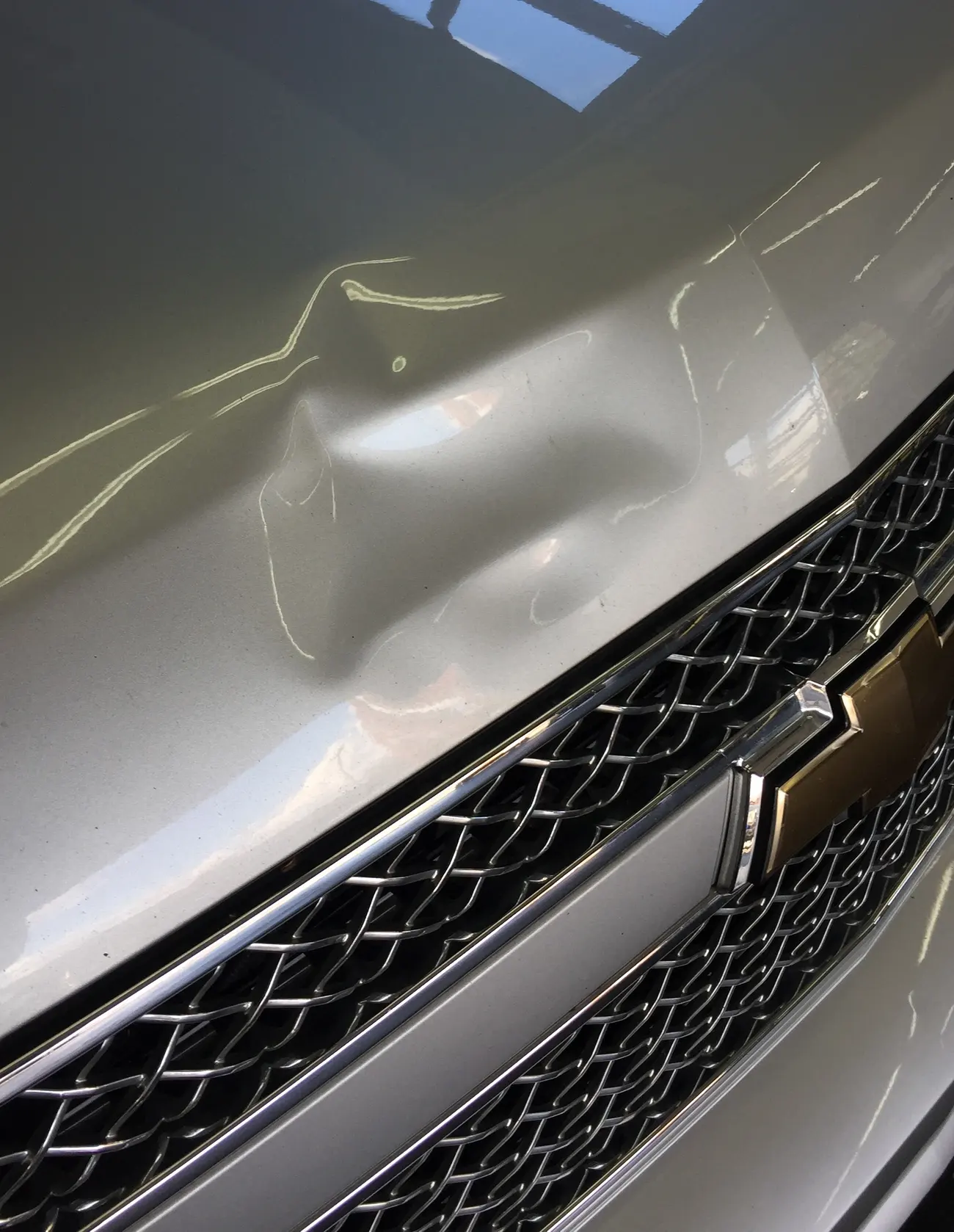 A dent in the hood of a Chevrolet before paintless dent repair