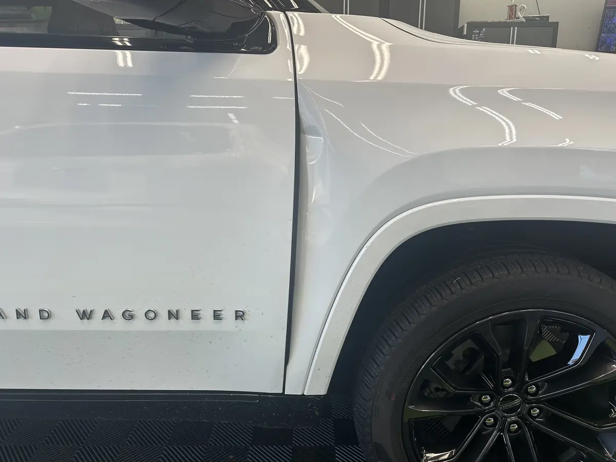 A dent in the front fender of a white Jeep Grand Wagoneer before repair