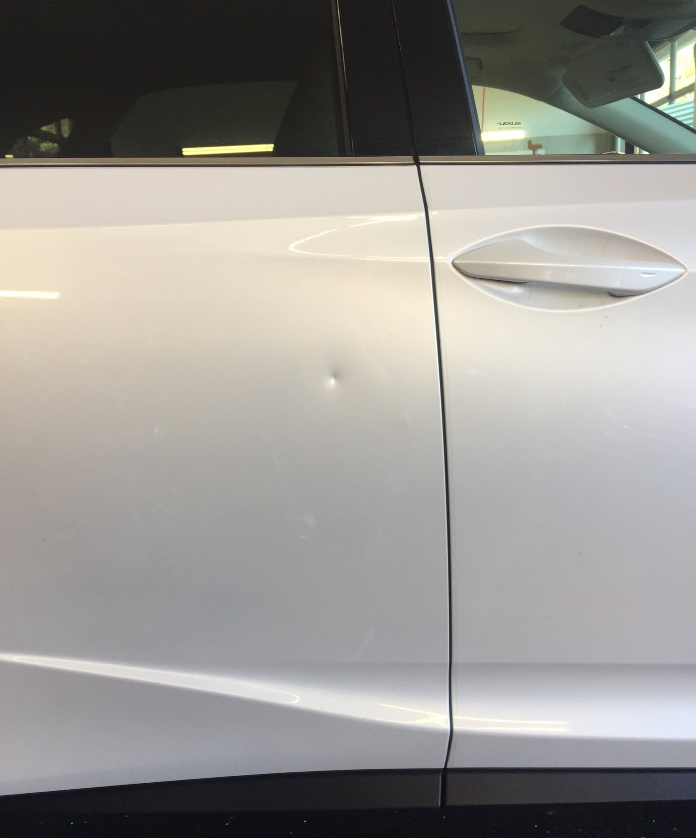 A round door ding in the flat of a silver Lexus door before paintless dent repair in Bellevue