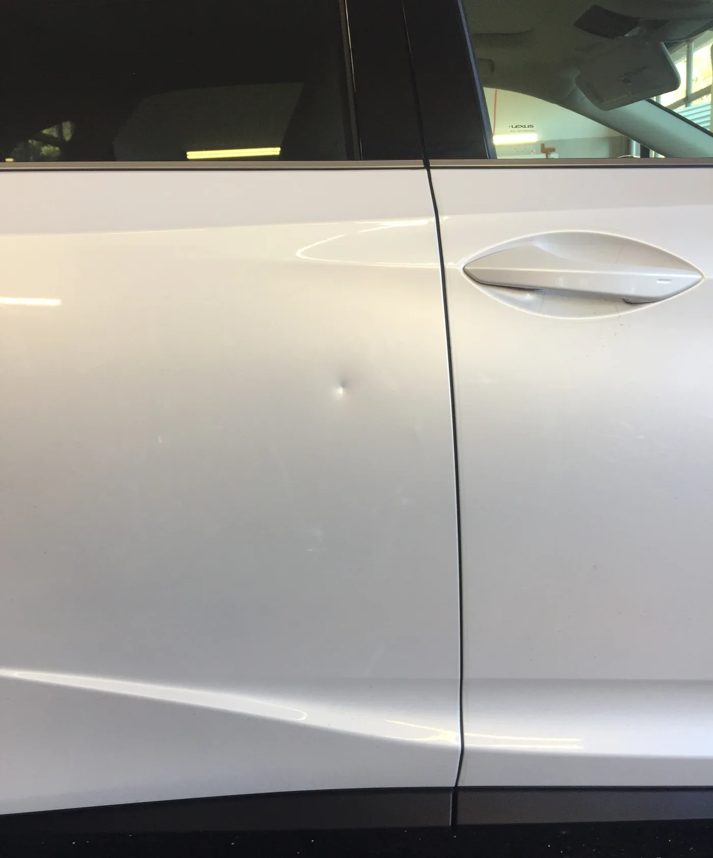 A round door ding in the flat of a silver Lexus door before repair