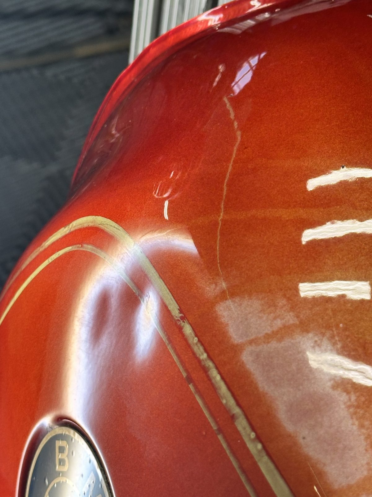A dent in the copper fuel tank of a motorcycle before paintless dent repair in Bellevue