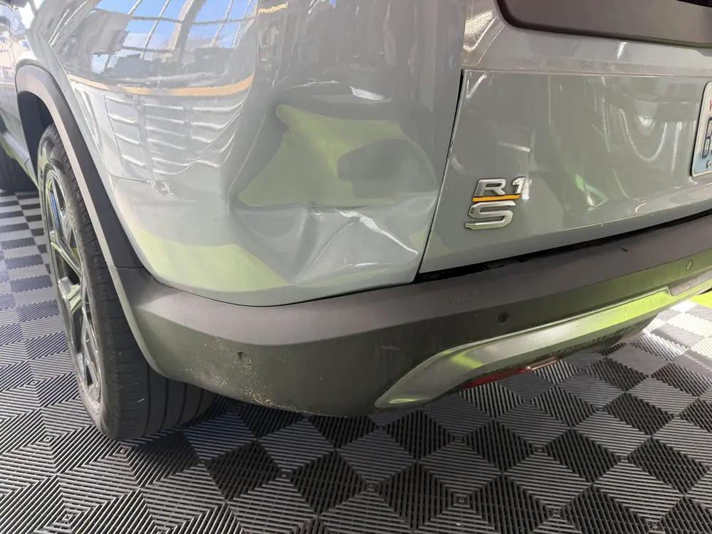 A dent low in the rear quarter panel of a gray Rivian R1S in the Bellevue shop
