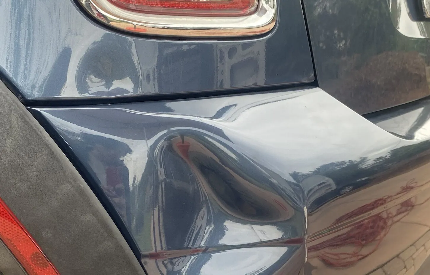 A deep dent in the corner of a gray plastic rear bumper before repair