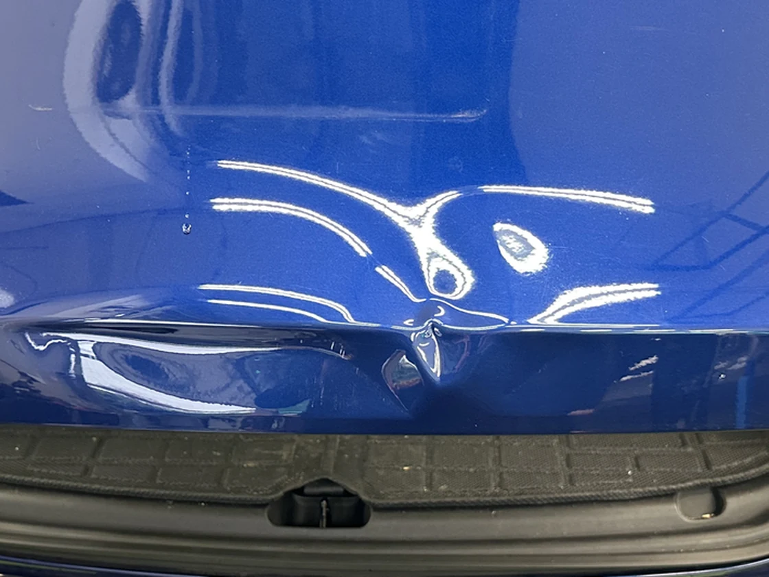 A dent in the tailgate of a blue Tesla Model Y before paintless dent repair