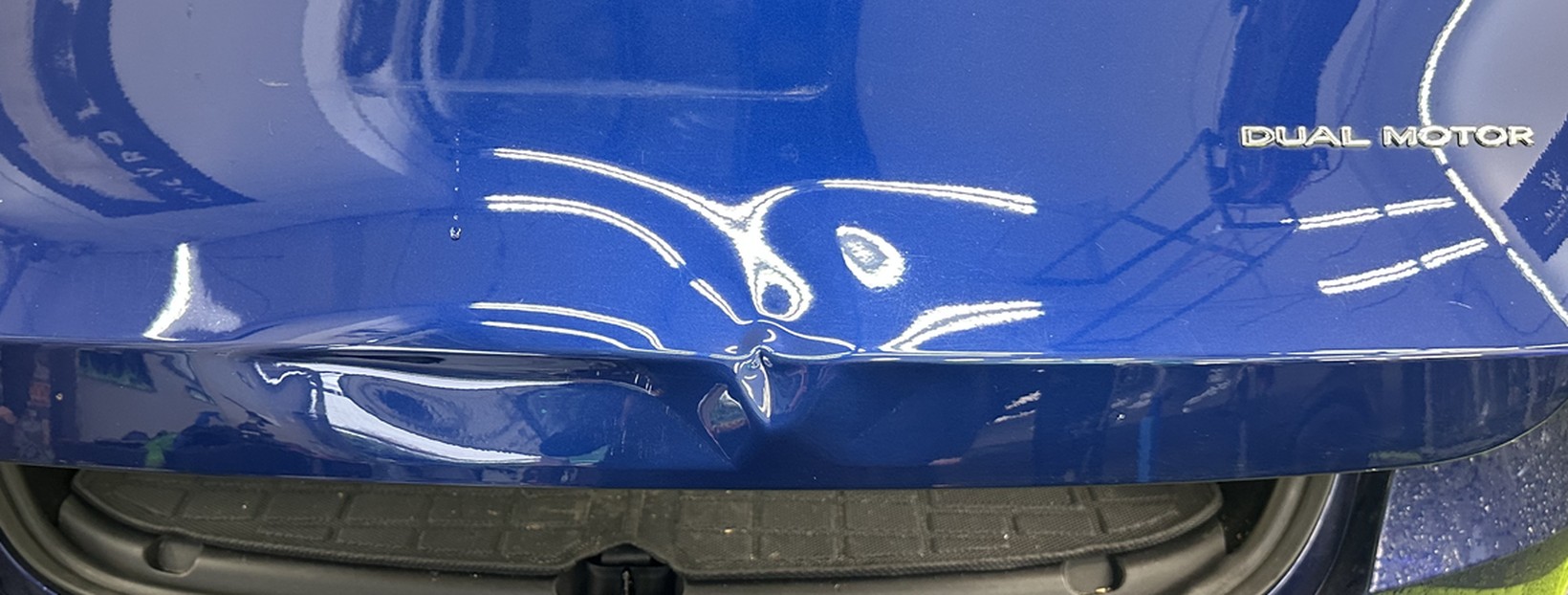 Dent running into the body line on the rear tailgate of a blue Tesla Model Y before repair